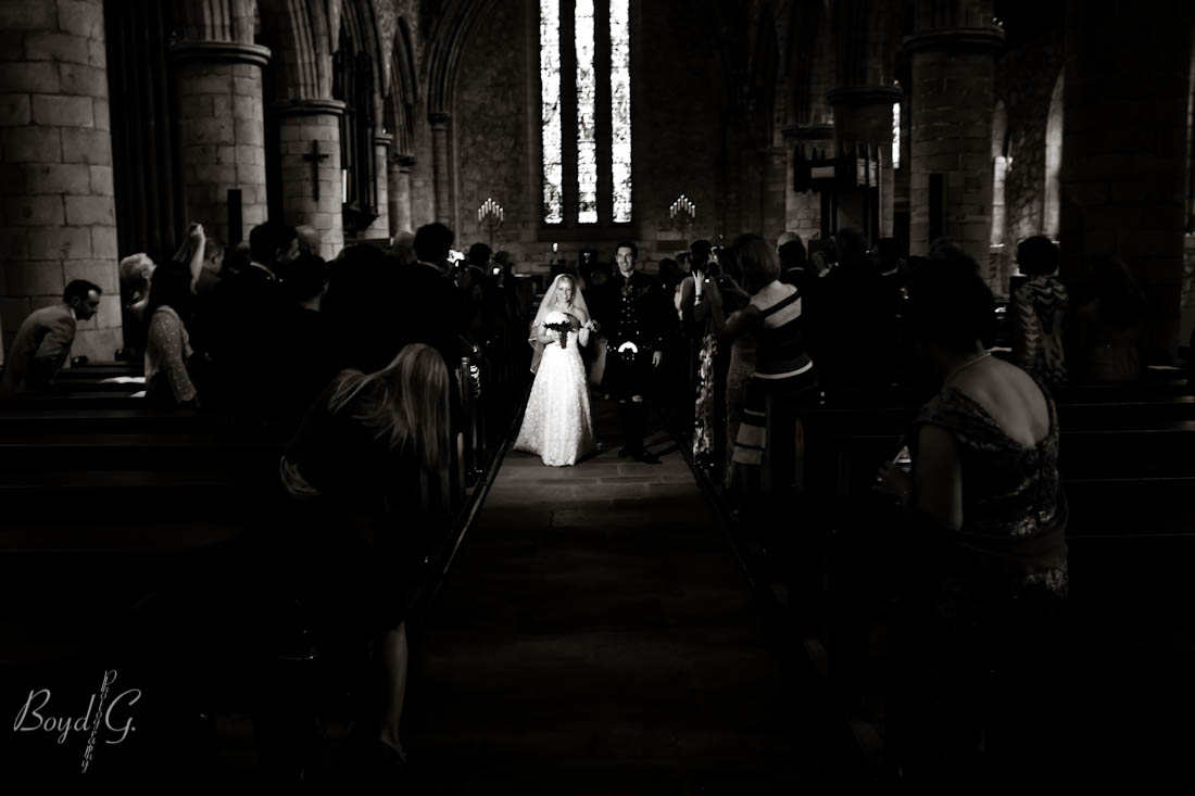 Bride and groom walk down the isle after being married, flash illuminates the couple in the dark surrounding church.